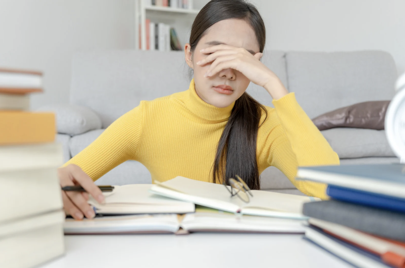Woman sitting at messy desk covering her face with her hand